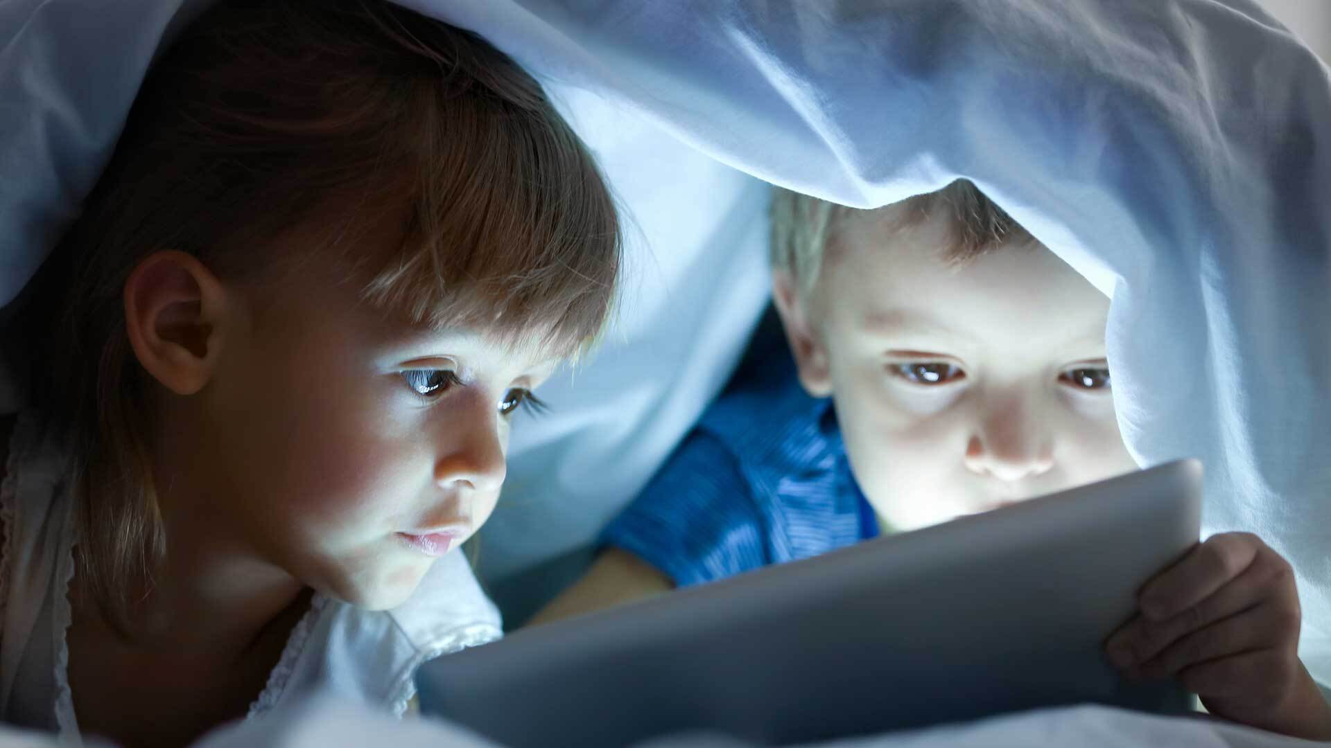 two kids under a blanket looking at a tablet
